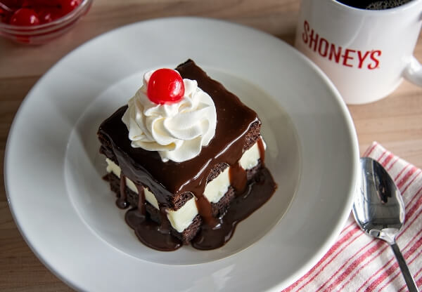 Hot fudge cake topped with whipped cream and a cherry, with fudge running down the sides.
