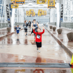 Child in a red hoodie with his arms up as he runs across the finish line in the rain.