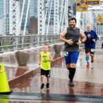 Two men and two children running across the finish line in the rain on a bridge.