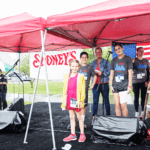 5k runners standing under a red tent after a performance.