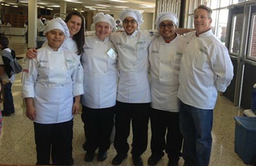 Several chefs standing next to each other smiling in the kitchen.